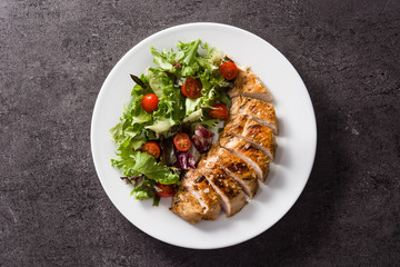 Grilled chicken breast with vegetables on a plate on black background. Top view
