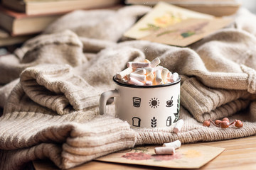 Marshmallows in a cup and a warm sweater on a wooden table background. Winter mood, Sunday...