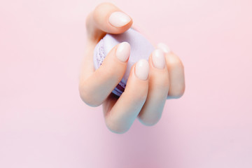 Girl holds hands violet macaron cookies through hole. Stylish trendy female manicure on pink background