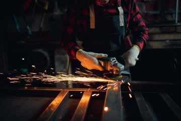 Woman working with angle grinder cuts and polishes metal after welding with spark
