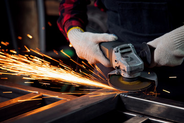 Worker hand with electric wheel grinding on steel structure in factory, light spark