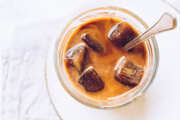 Pouring milk from a jug to a glass of espresso ice cubes