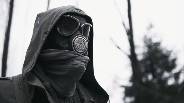 Male wanderer in protective gas mask walking in empty dark forest. Stalker concept, portrait of lonely survivor after nuclear or chemical war. Post apocalyptic world. Stedicam following shot