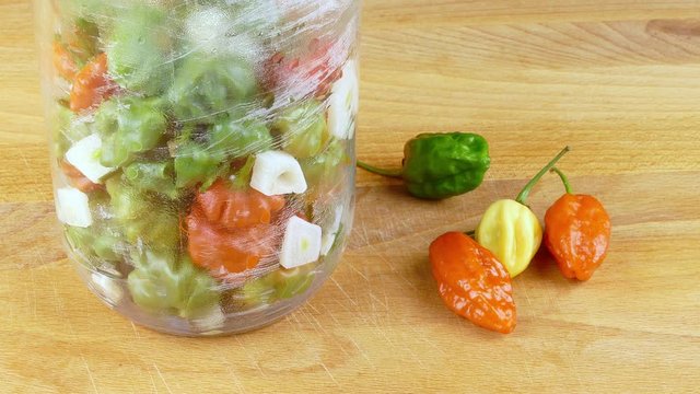 pouring blanched hot chili peppers with hot vinegar at preparation of pique sauce, a Puerto Rican hot sauce