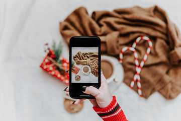 Woman's hand take a mobile photo of christmas composition with hot coffee. Smartphone with mobile...