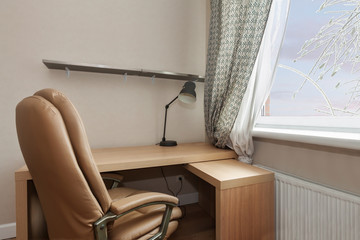 Close up view of home office with wooden work desk beige pastel color interior with armchair and lamp window curtains cold winter day background.