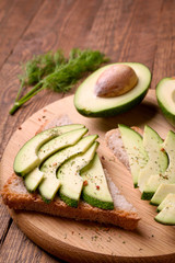 Beautifully plated avocado toast with delicious-looking toppings on wooden brouw background. Making sandwiches with avocado healthy organic food top view.On A Wooden Cutting Board Sliced avocado.