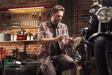 Mechanic kneeling working on a vintage motorbike - 302266889