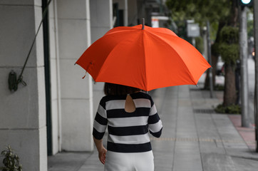 Back view of woman with orange umbrella walking on a street.