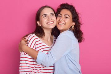 Two pretty sisters or friends women with dark hair, wearing casual shirts. Girls hugging over pink...