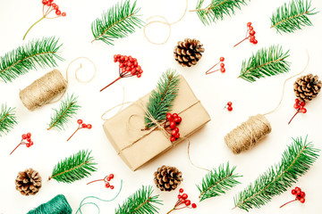 Christmas flat lay in dynamics. Different baubles and fir branches move diagonally. A large gift box with wrapping paper in the center of the image.