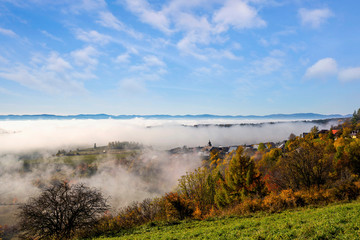 Scenic view of beautiful autumn rural landscape with small village in front of morning fog, Slovakia..