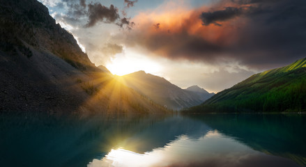 Fototapeta na wymiar Panoramic view landscape with illuminated mountain peaks, rocks in a mountain lake, reflection, blue sky and yellow sunset sunshine.