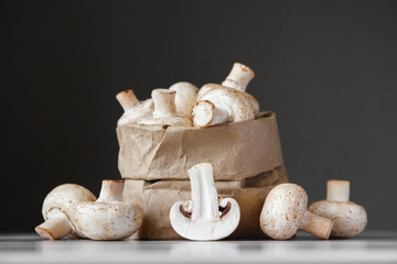 Mushrooms champignons in paper bag on a white wooden table on a dark background. Place for text or advertising