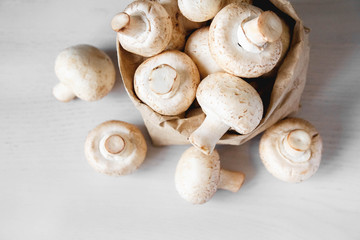 Mushrooms champignons in paper bag on a white wooden table. Place for text or advertising. Top view
