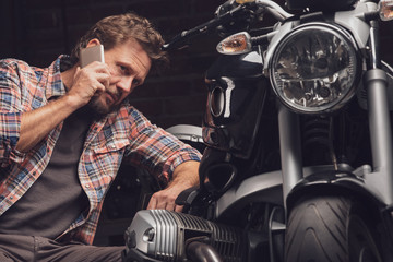 Man talking by the phone kneeling at motorcycle - 302270273