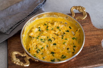 Scrambled eggs with cheese and spring onion. Served in a copper pan.