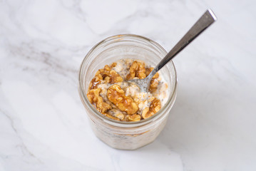 Overnight oats with chia seeds, walnuts and yogurt, on a white marble background.