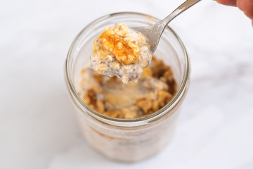 Overnight oats with chia seeds, walnuts and yogurt, on a white marble background.