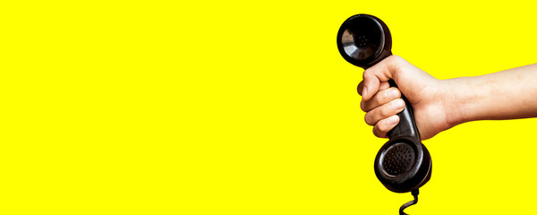 Hand holding old telephone receiver on yellow background.
