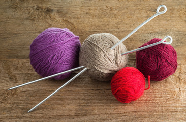 Balls of yarn in different colors with knitting needles on a background of rough wood texture.