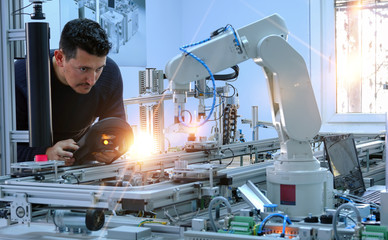 Man is programming robotic arm with control panel which is integrated on smart factory production...