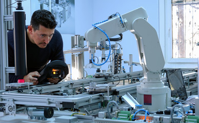 Man is programming robot arm with control panel which is integrated on smart factory production...