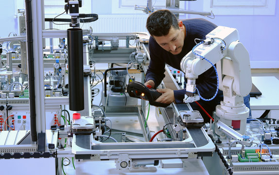 Man is programming robot arm with control panel which is integrated on smart factory production line. industry 4.0 automation line which is equipped with sensors and robotic arm. Selective Focus.