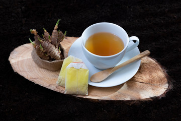 A cup with an infusion of turmeric alongside its sprouting seeds standing on a log of pine tree with a soil background - Glycyrrhiza glabra