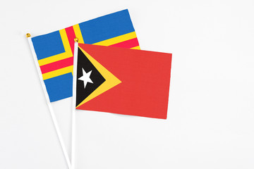 East Timor and Aland Islands stick flags on white background. High quality fabric, miniature national flag. Peaceful global concept.White floor for copy space.