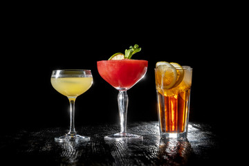 Three cocktails, Strawberry daiquiri, Long island and daiquiri on black background.