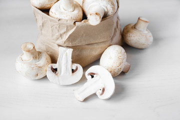 Mushrooms champignons in paper bag on a white wooden table. Close up. Place for text or advertising