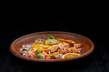 Grilled salmon and vegetables. Laid on a beautiful clay plate, sprinkled with onions, dill and tomatoes.