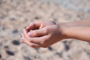 Sand spills out of the hands. On the beach near the sea