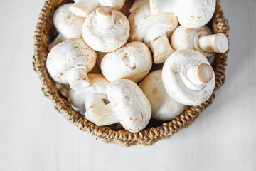 Mushrooms champignons in a round wicker basket on a white wooden table. Place for text or advertising. Top view