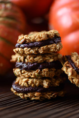 Healthy vegan dessert. Pile of homemade pumpkin oatmeal breakfast cookie sandwiches with dark chocolate and winter squashes on oak board