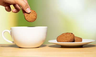 Hand hold cookies dipping coffee on wooden table and blur background