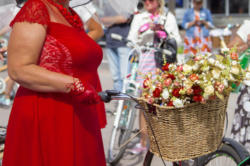 Woman in a red dress and gloves holds the bike wheel. Basket with roses. Frame part.