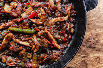 Stir fry vegetables and meat in cast iron skillet with soy sauce and spices flat lay on a wooden table