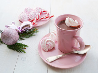 Obraz na płótnie Canvas Cup of cocoa with swirled peppermint meringue cookies in pink mug over white table. Christmas decorations in the background.