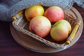 Beautiful ripe apples in a wicker basket on a wooden background.