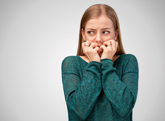 Young beautiful girl with long ginger hair wearing green sweater isolated on white background. Frightened nervous woman, keeps hands near mouth, looks with shock at aside to place of advertising