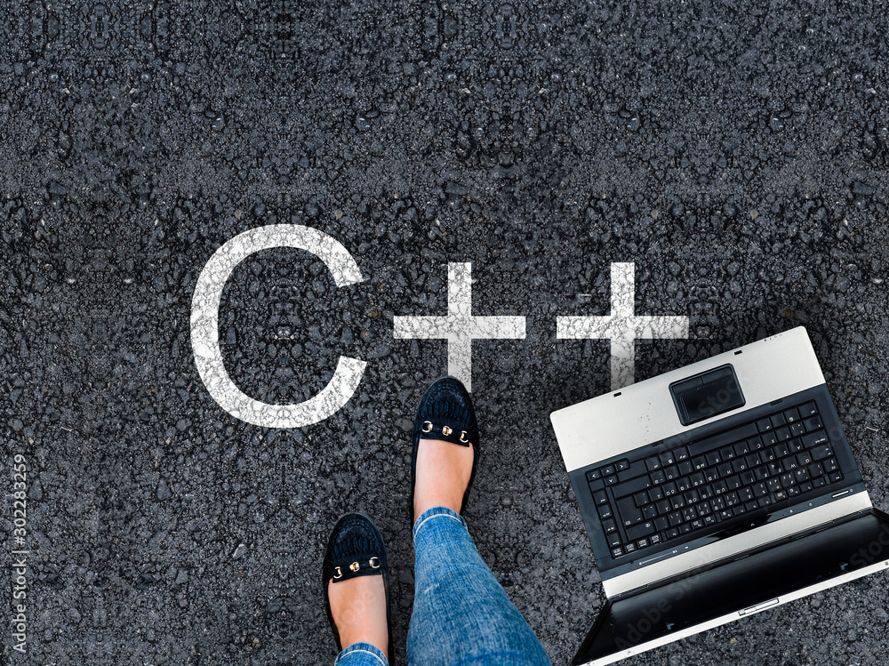 Wall mural c++ programming language. .a woman steps to a laptop and c++ on asphalt road