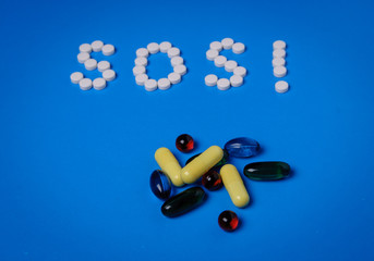 SOS from pills and capsules with medicine on a blue background. Addiction and prevention concept