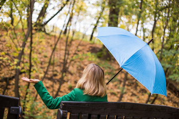 Woman holding blue umbrella and checking for rain while sitting in the park.