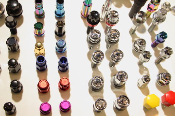 More rows multi colored wheel nuts and bolts on white backdrop close up, technical texture for background