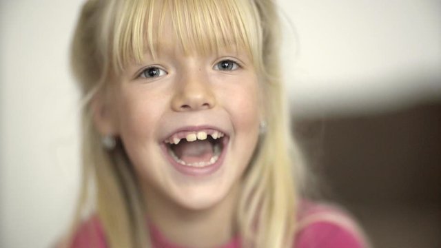 Face close-up portrait. blonde, beautiful little girl looking at the camera and laughing. no teeth