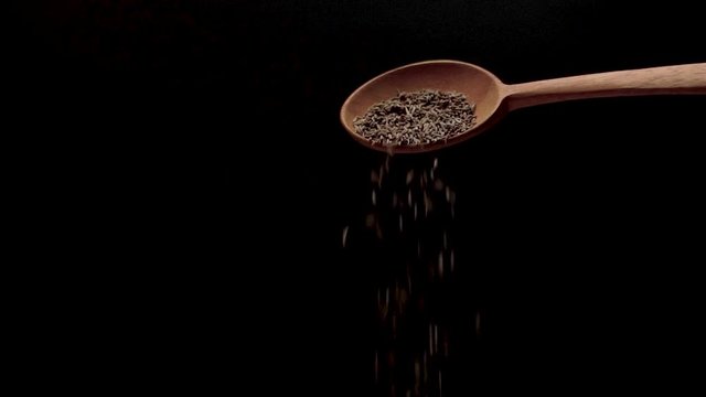 Slow motion of cumin seed poured slowly from a wooden spoon