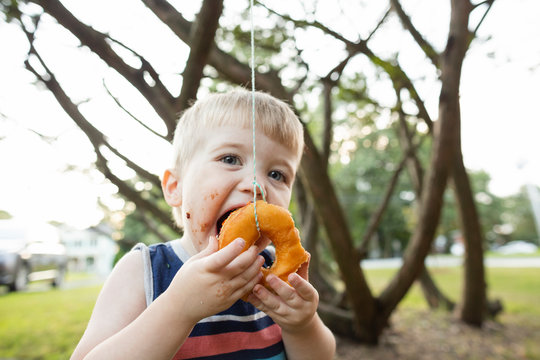Happy playful toddler boy opens mouth to bite donut during party game