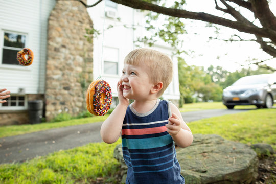 Happy toddler boy smiles while trying to eat donut during party game